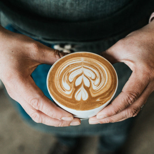 hands holding a cup of cappuccino with pattern in froth milk