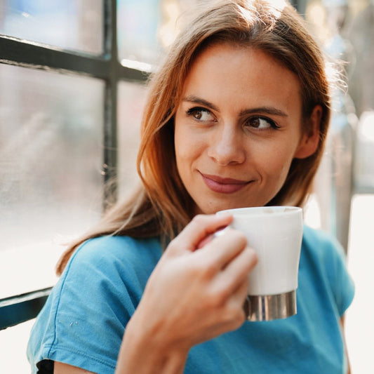 women standing at window with a cup of fresh roasted brewed coffee in her hand