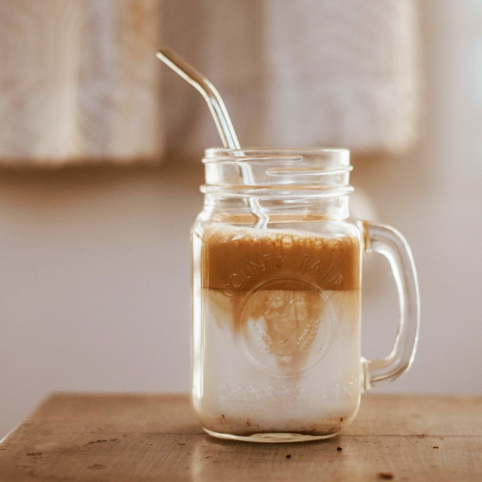glass mug of cold brew coffee with cream and straw on a table