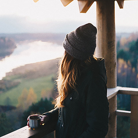 woman looking over scenic vista while travelling with coffee